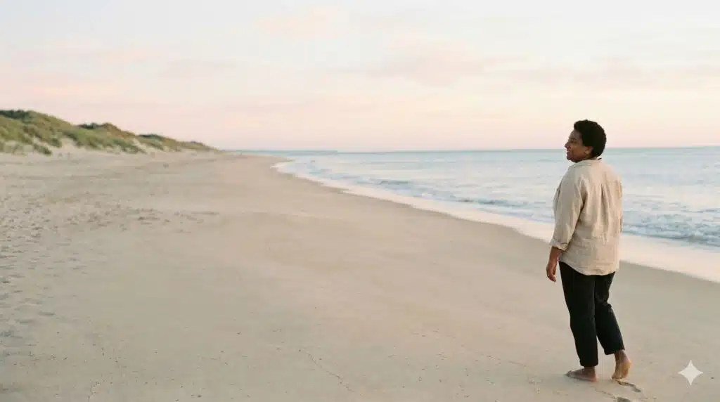 Femme sereine marchant sur une plage au coucher du soleil pour illustrer l'art de se retrouver et de faire de soi une priorité.